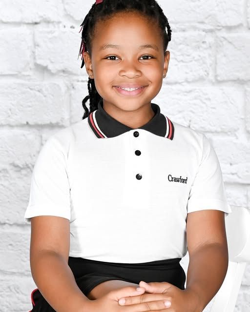 Girl wearing a white collared shirt with black trim, smiling, against a white brick wall.