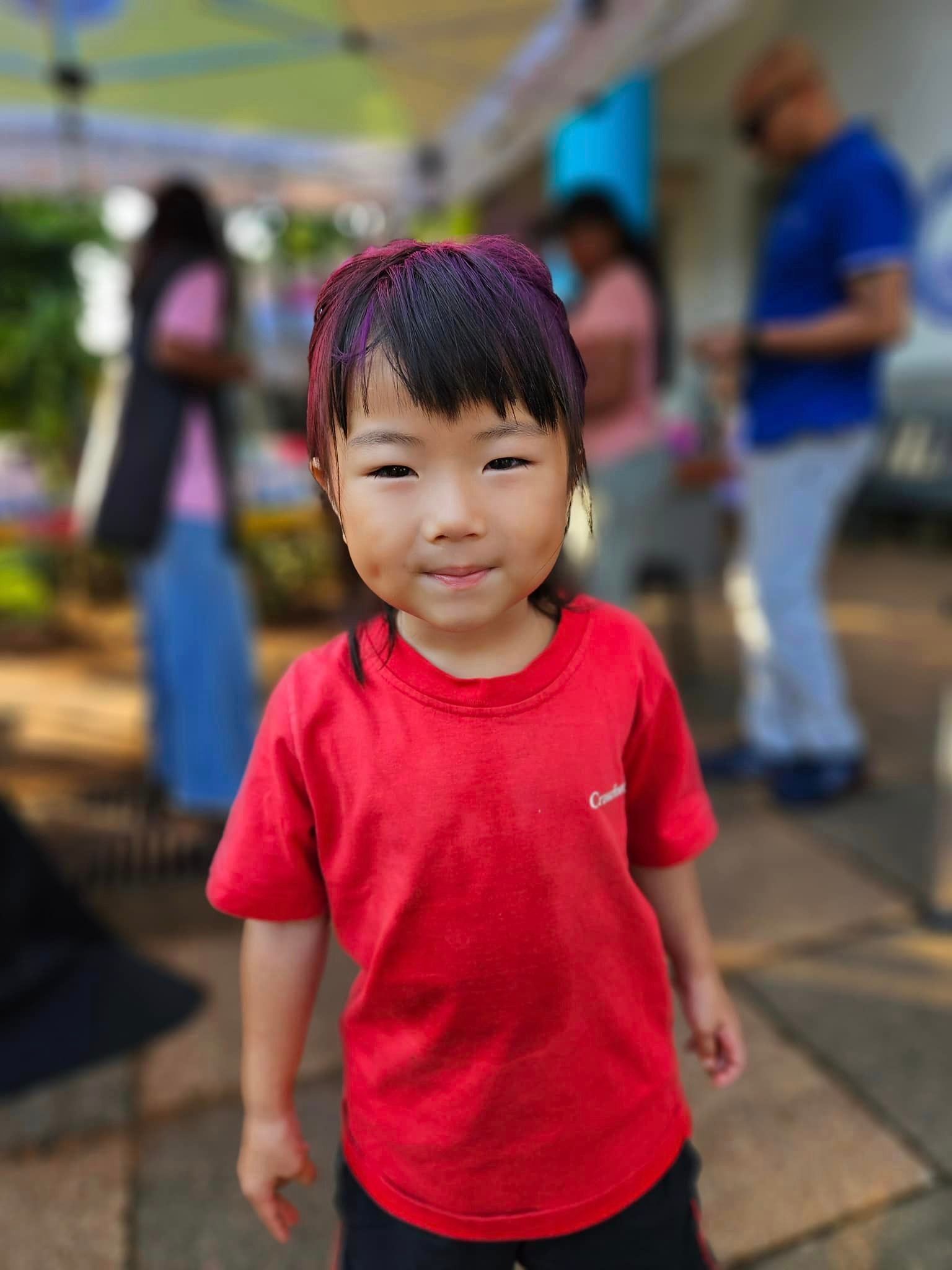 A little girl in a red shirt is standing on a sidewalk.