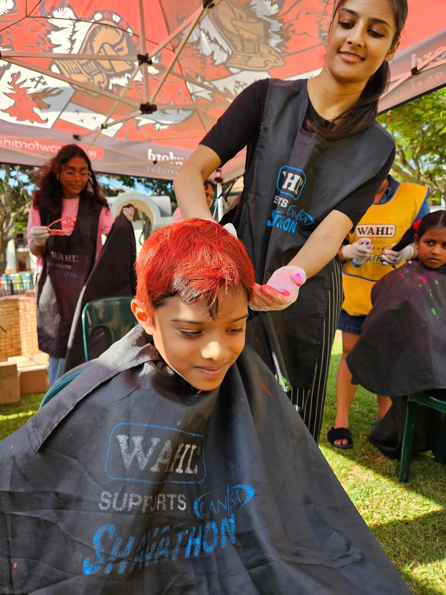 A young boy is getting his hair cut by a woman.