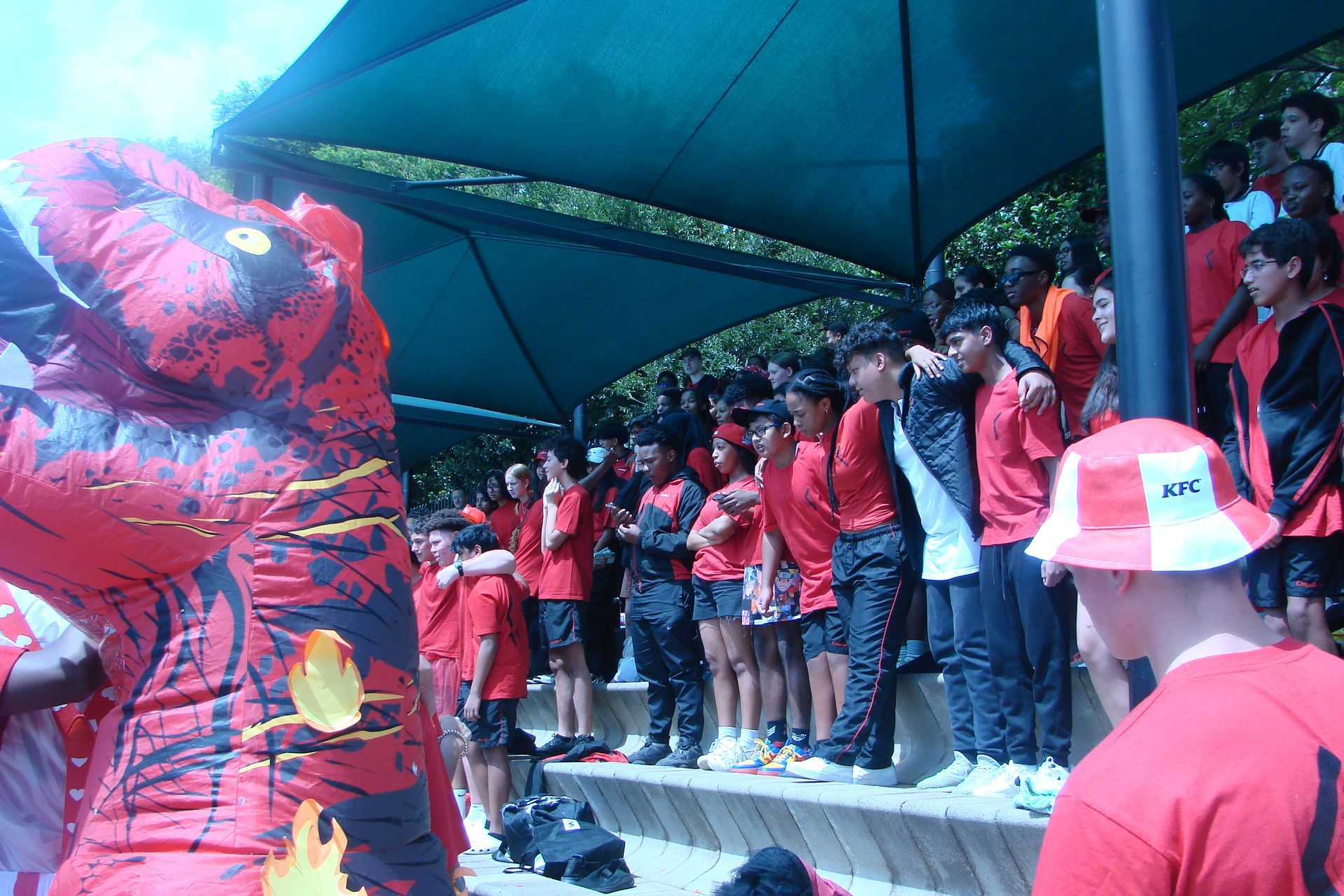 A group of people in red shirts are standing under an umbrella