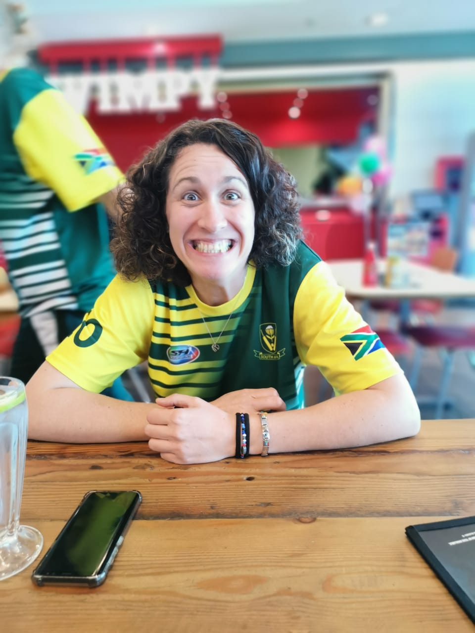 A woman is sitting at a table wearing a yellow and green shirt with the number 10 on it