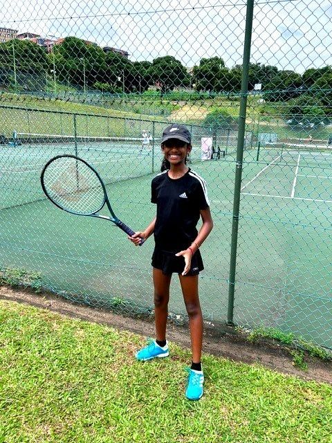 Young person holding a tennis racket on a tennis court, wearing athletic gear.