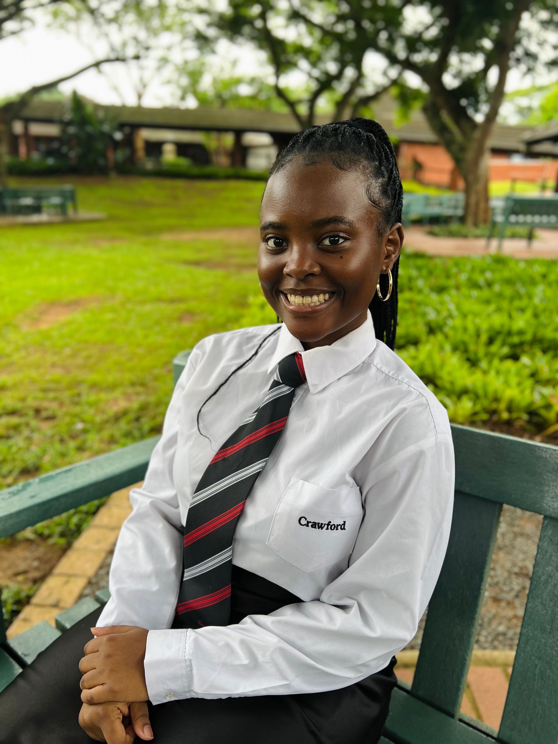 A young woman in a white shirt and tie is sitting on a bench.