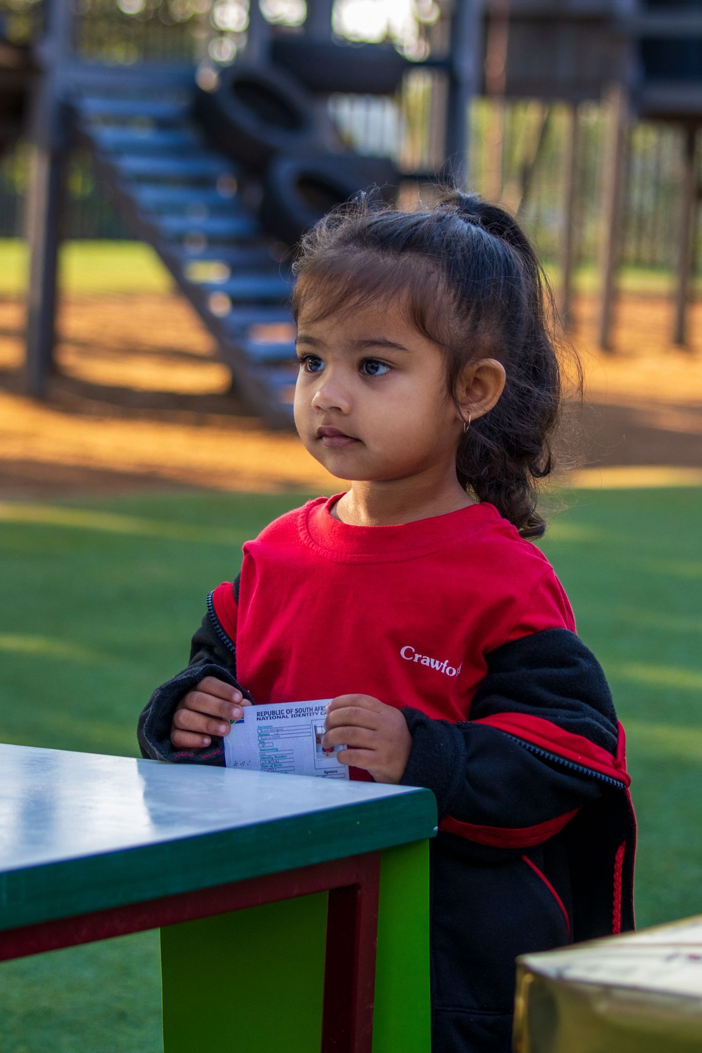 A little girl is sitting at a table in a park.