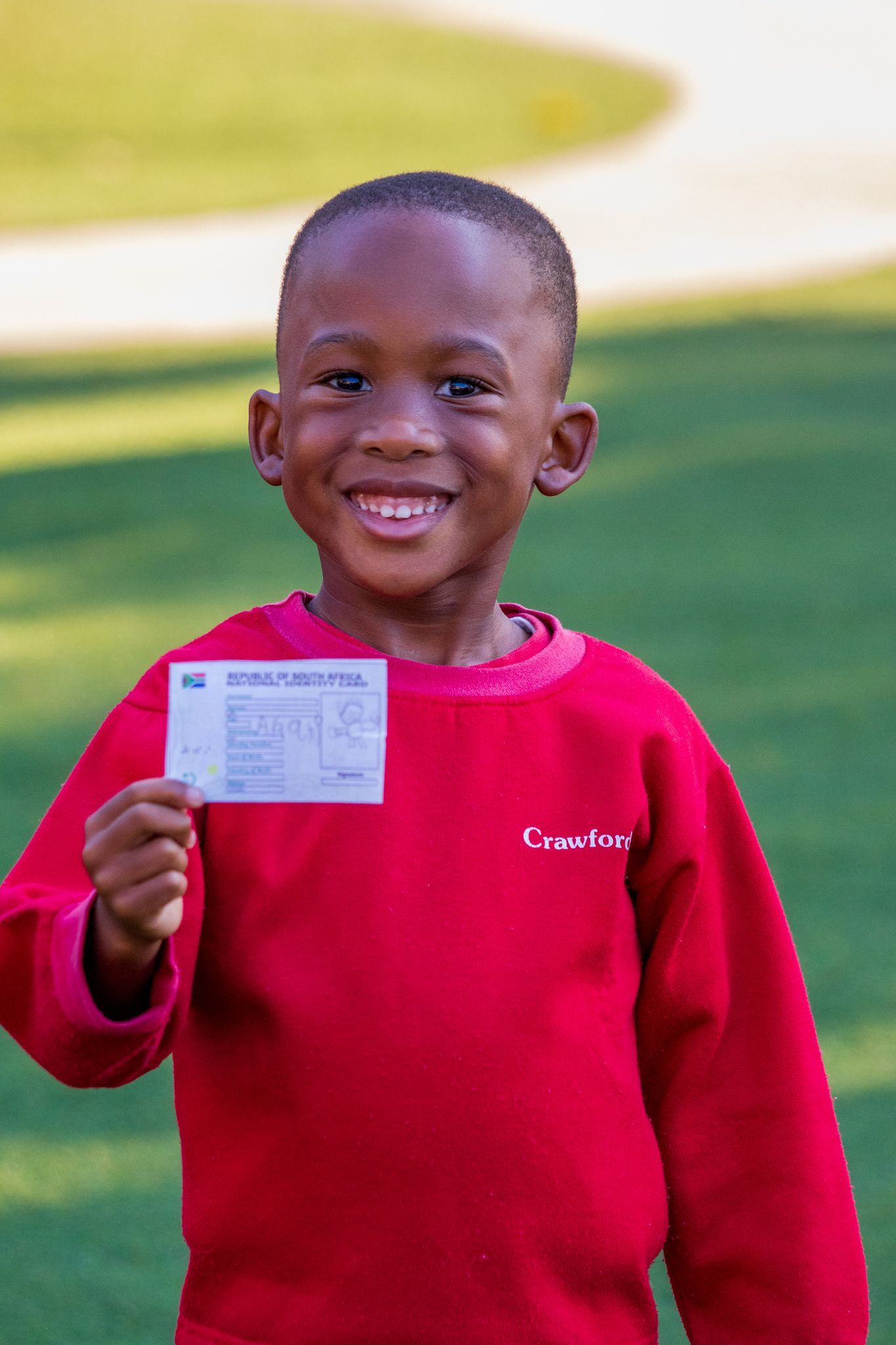 A young boy in a red sweater is holding a ticket and smiling.