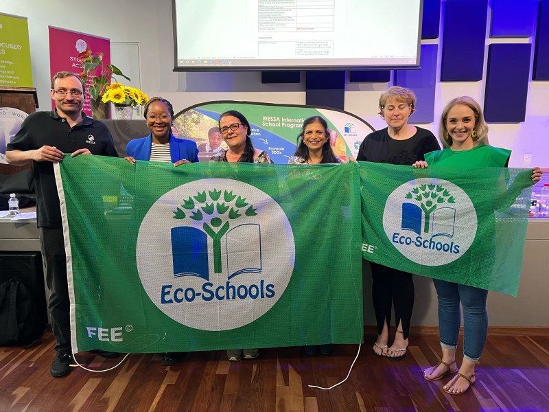 A group of people are holding a green eco-schools flag.