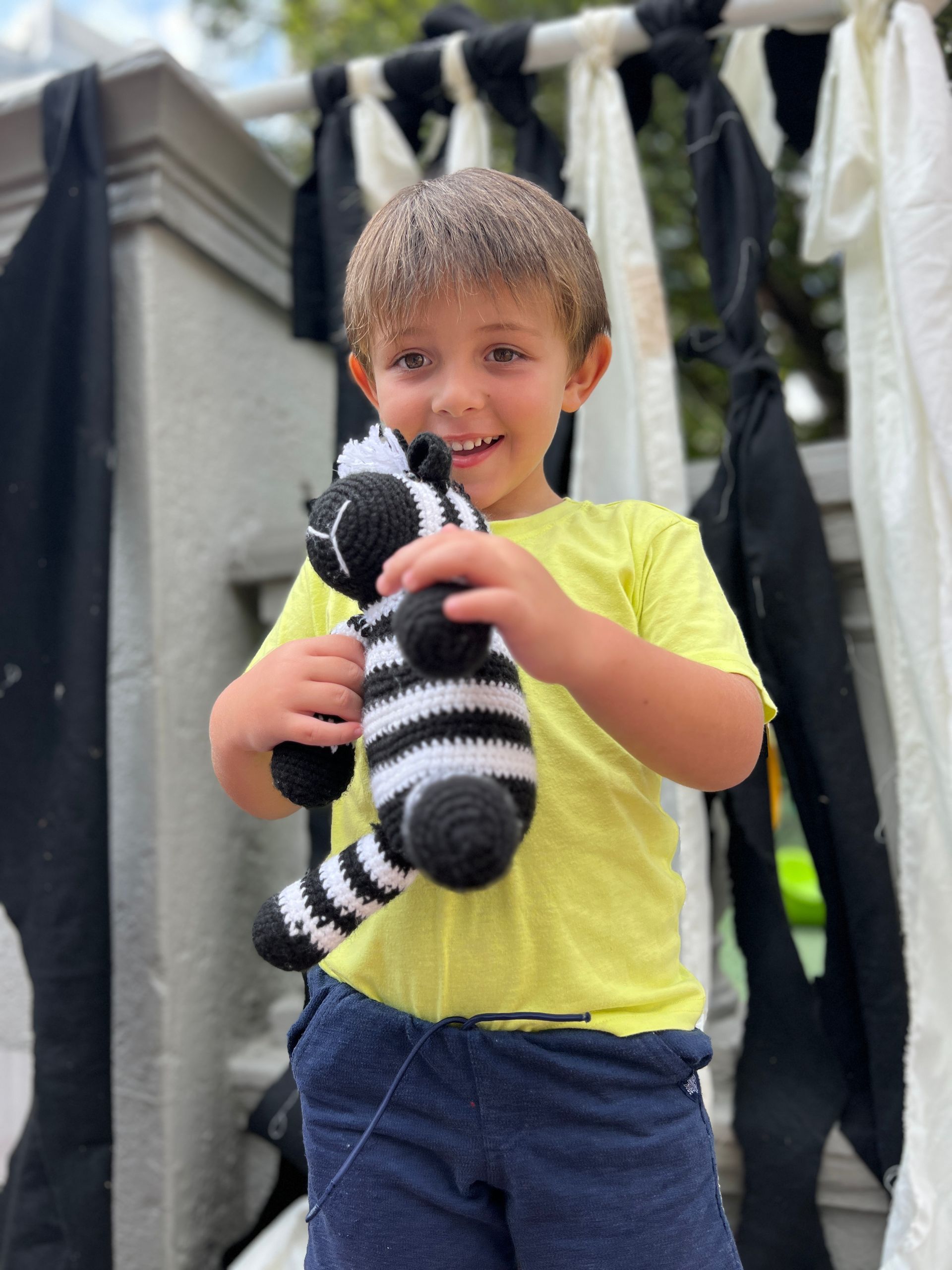A young boy in a yellow shirt is holding a stuffed zebra.
