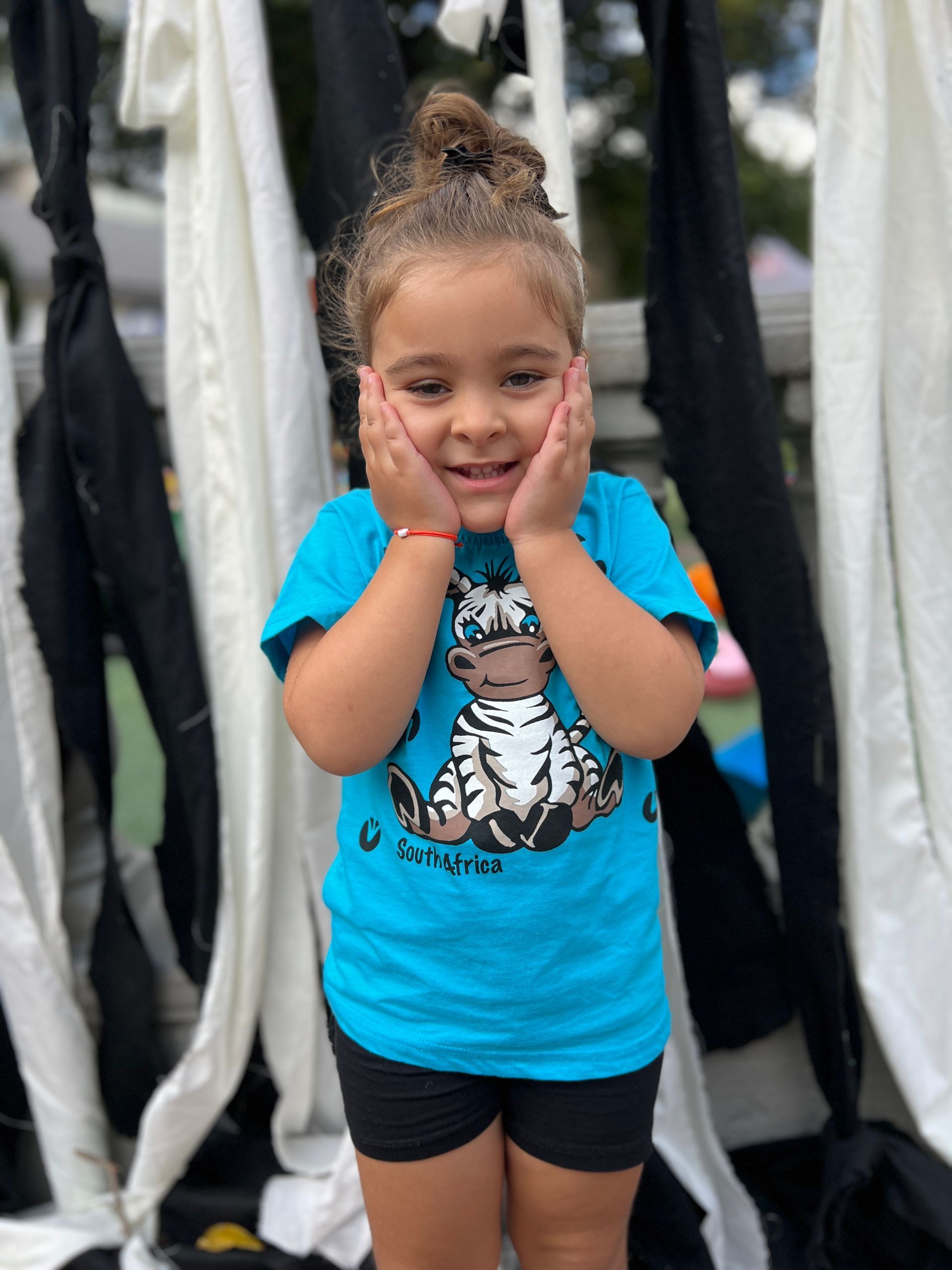 A little girl wearing a blue shirt with a cow on it is standing in front of a wall.