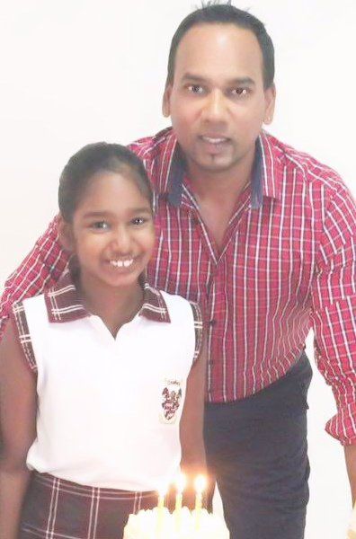 A man and a girl are posing for a picture in front of a birthday cake
