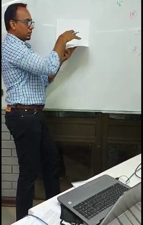 A man is standing in front of a white board holding a piece of paper.