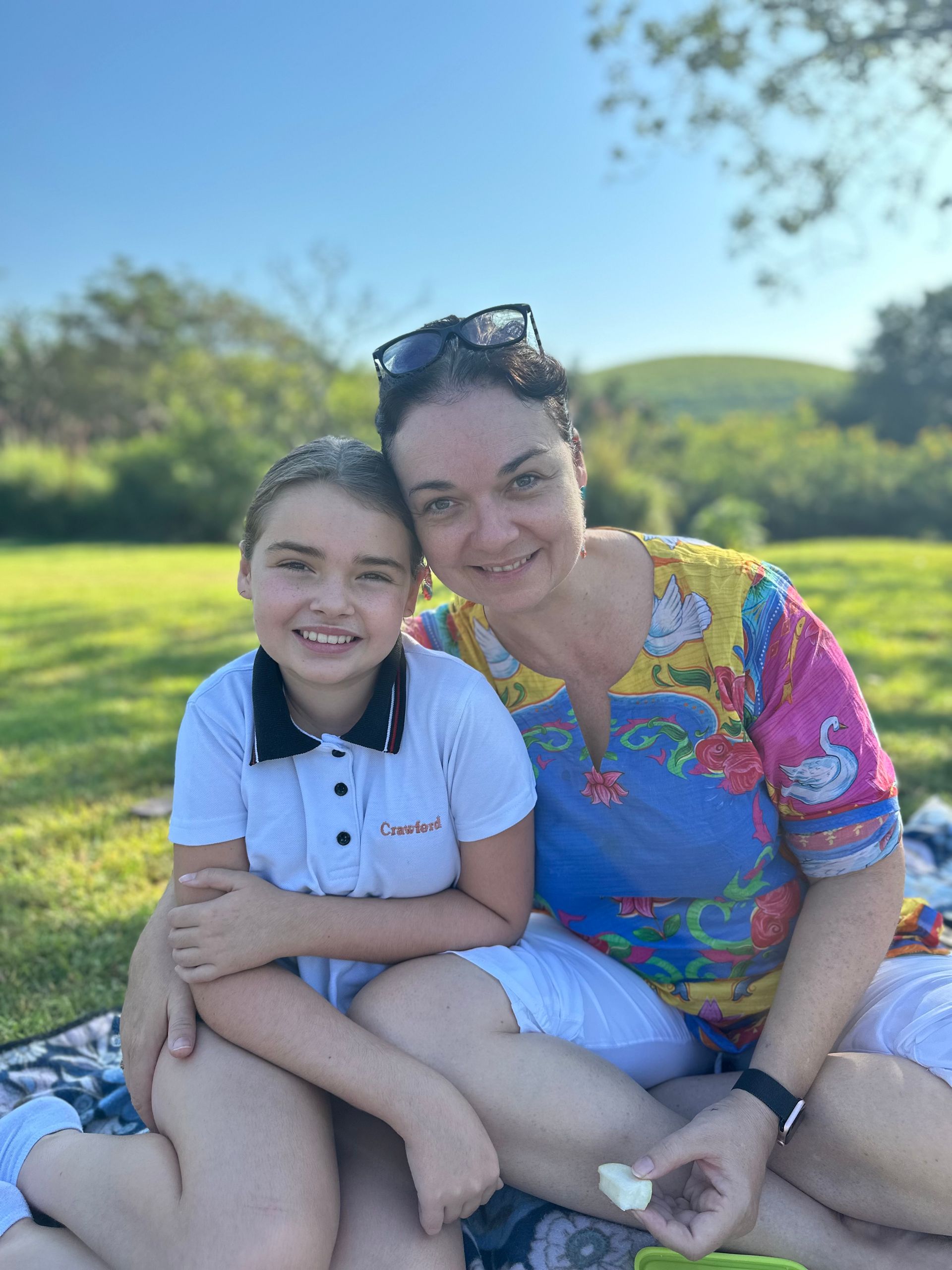 A woman and a child are sitting on a blanket in a park.