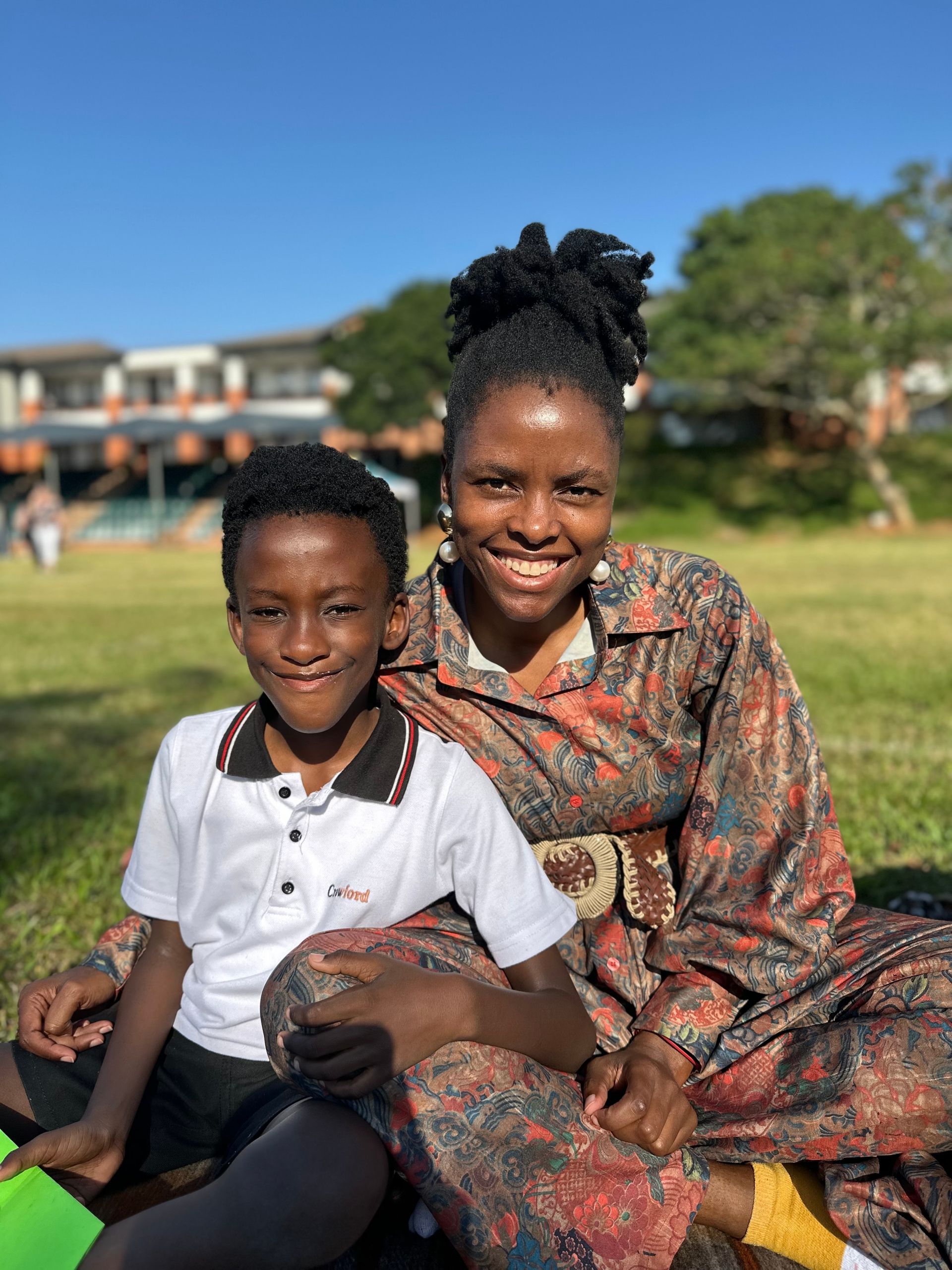 A woman and a boy are sitting on the grass in a park.
