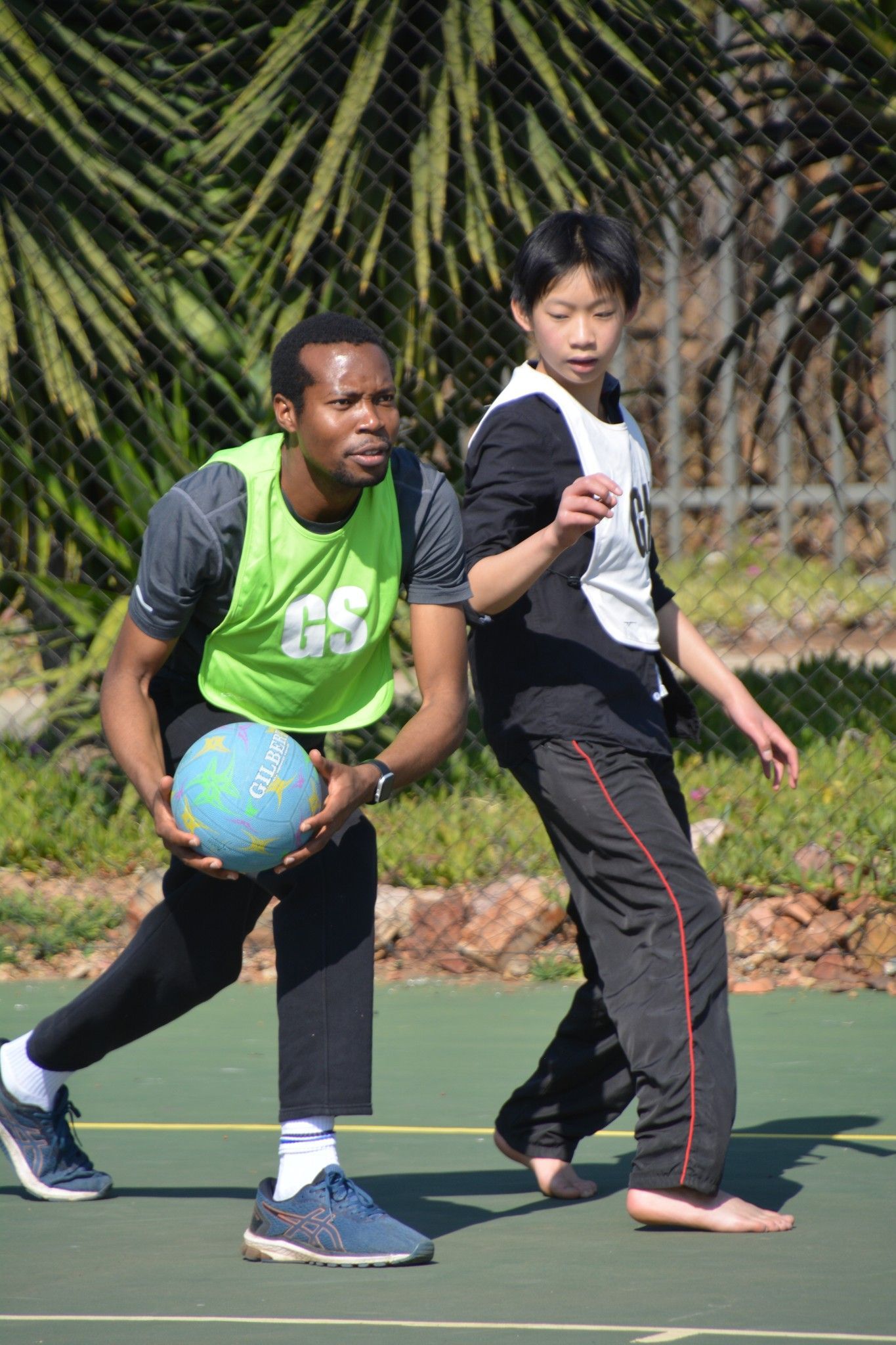 A man and a boy are playing a game of netball on a court.