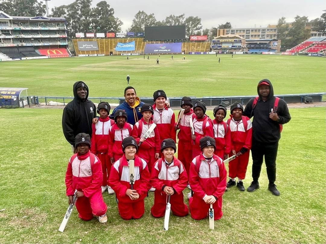 A group of children are posing for a picture on a cricket field.