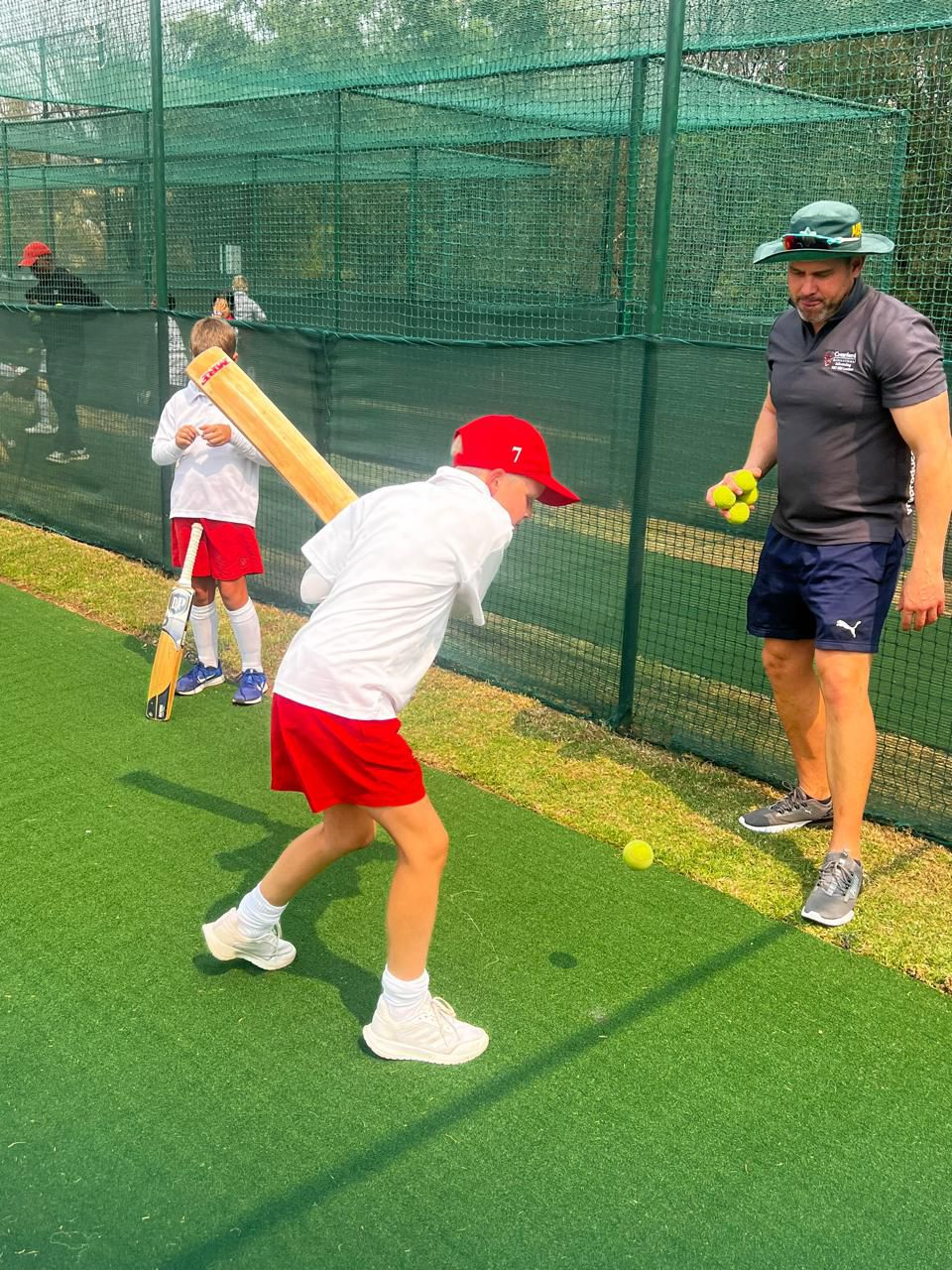 A man is teaching a young boy how to play cricket on a field.