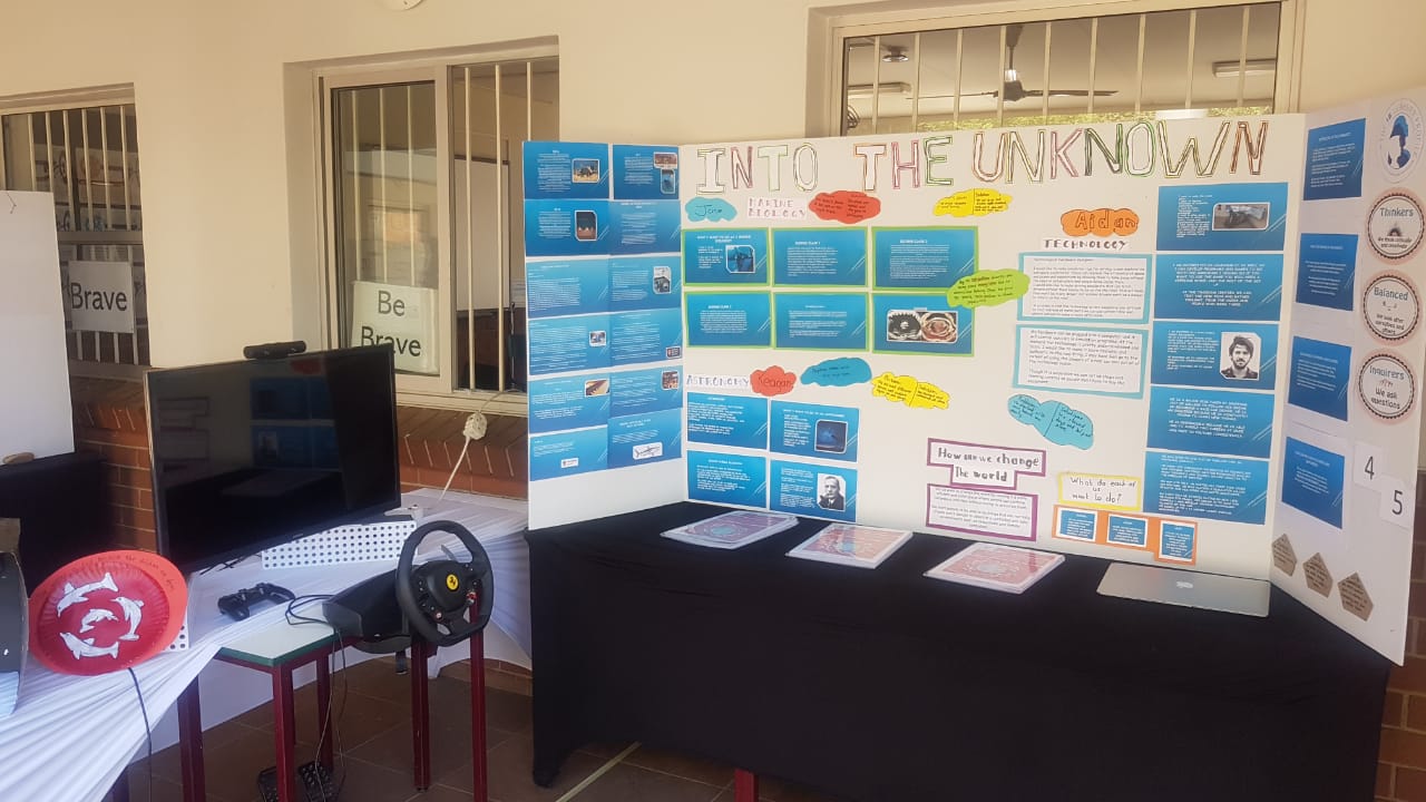 A room with a table , chairs , a steering wheel and a sign that says `` the unknown ''.