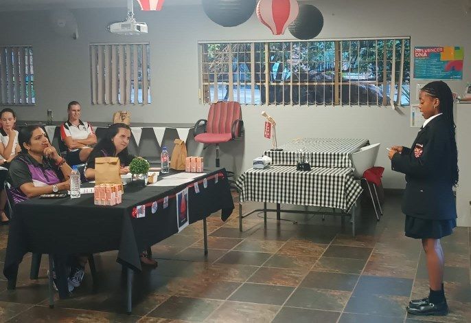 A girl is standing in front of a group of people sitting at tables.
