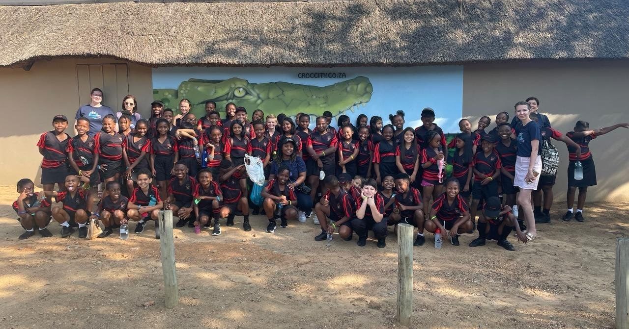 A large group of people are posing for a picture in front of a thatched roof.