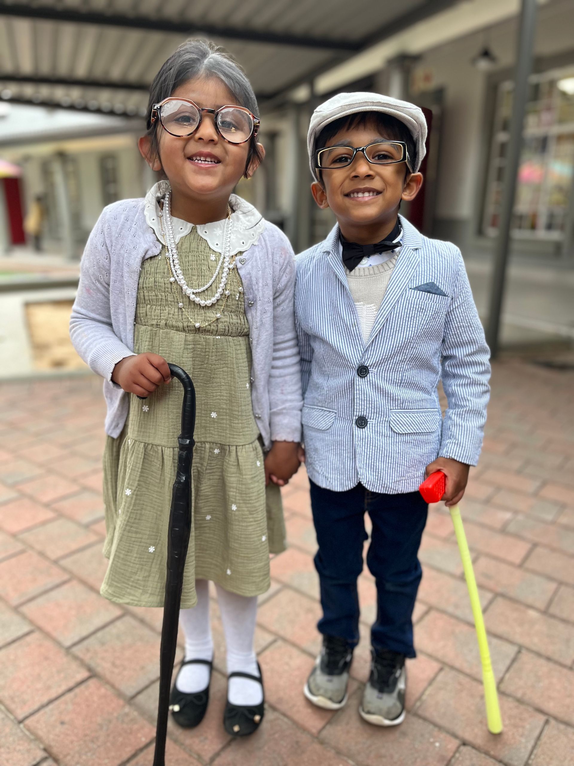 A boy and a girl are dressed up as grandparents and holding hands.