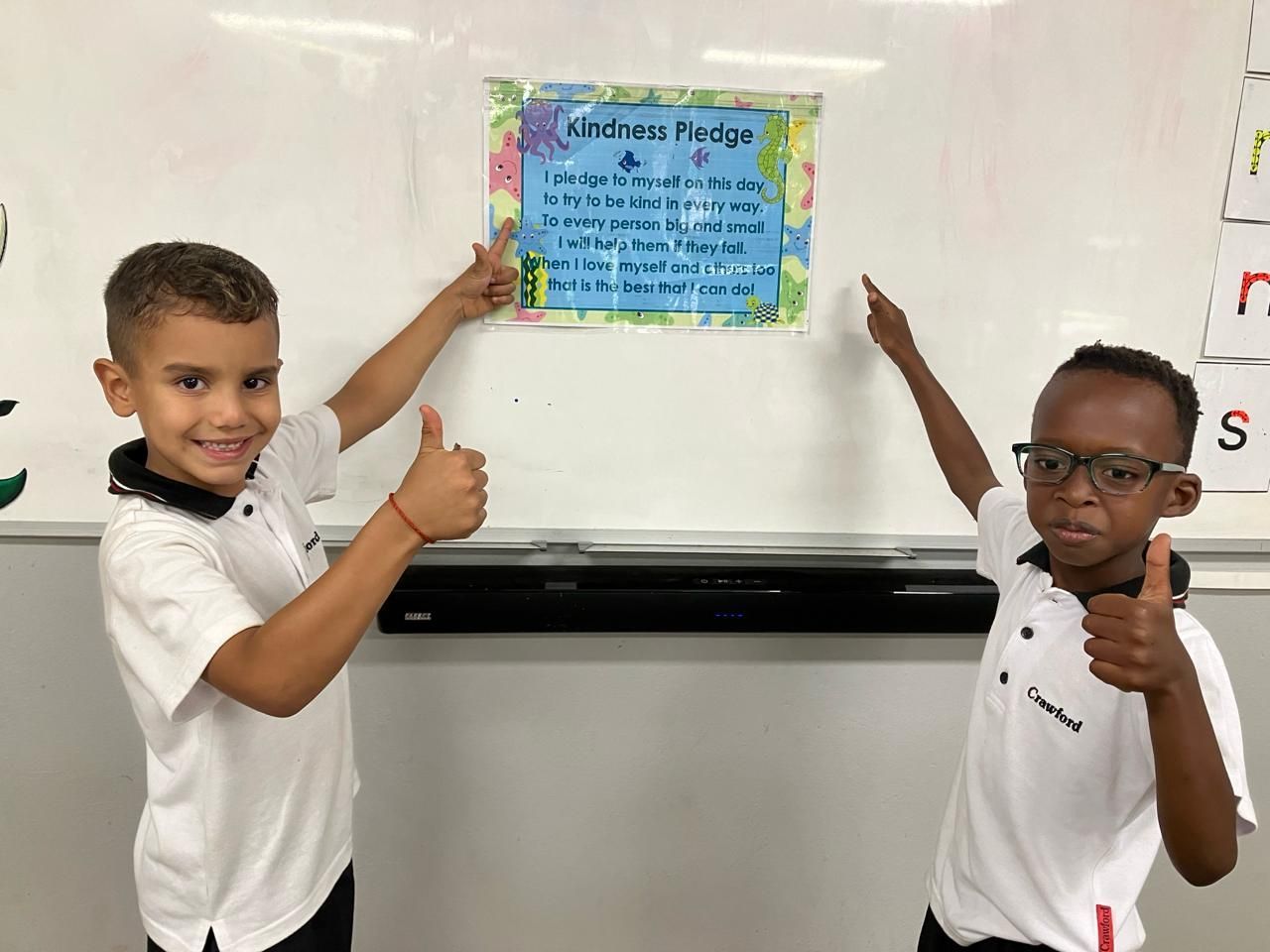 Two young boys are giving a thumbs up in front of a whiteboard.