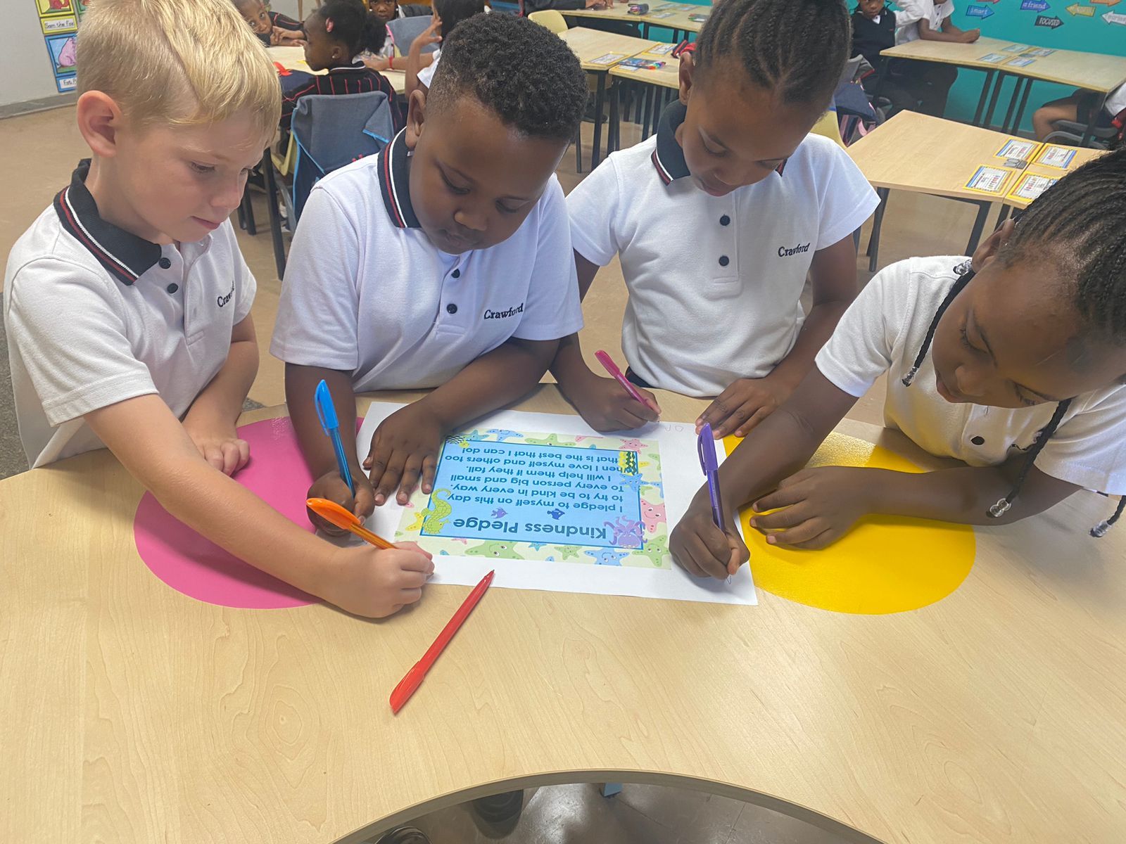 A group of children are sitting at a table drawing on a piece of paper.