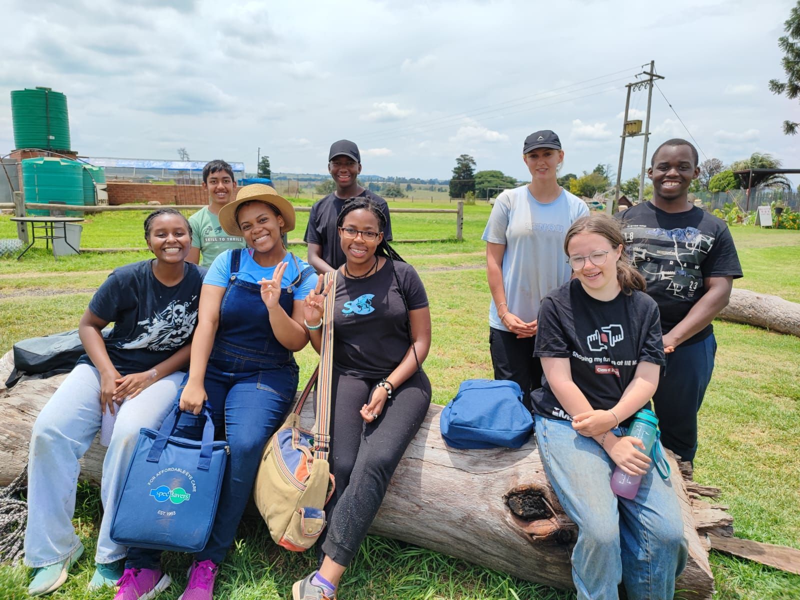A group of people are sitting on a log in the grass.