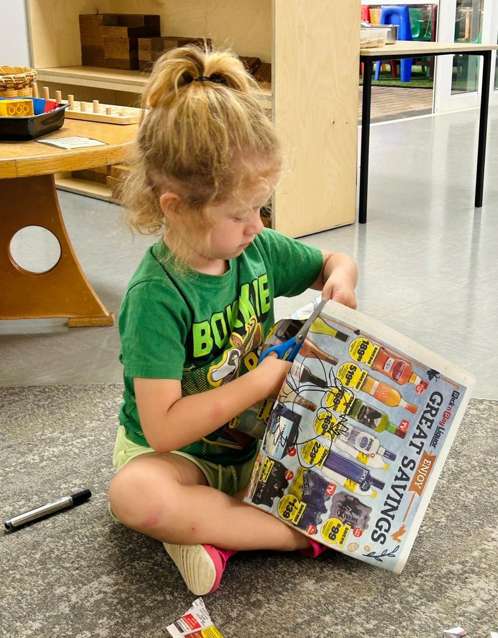 A little girl is sitting on the floor reading a magazine