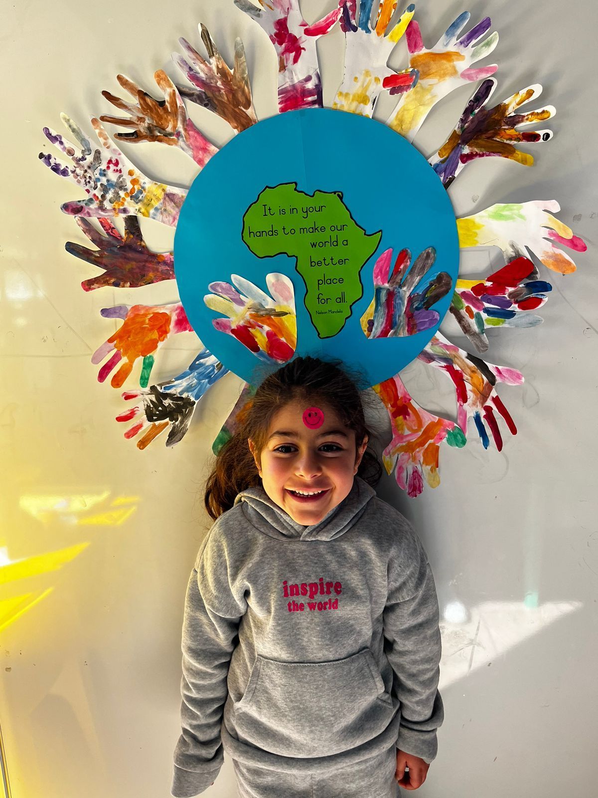 A little girl is standing in front of a globe made out of hands