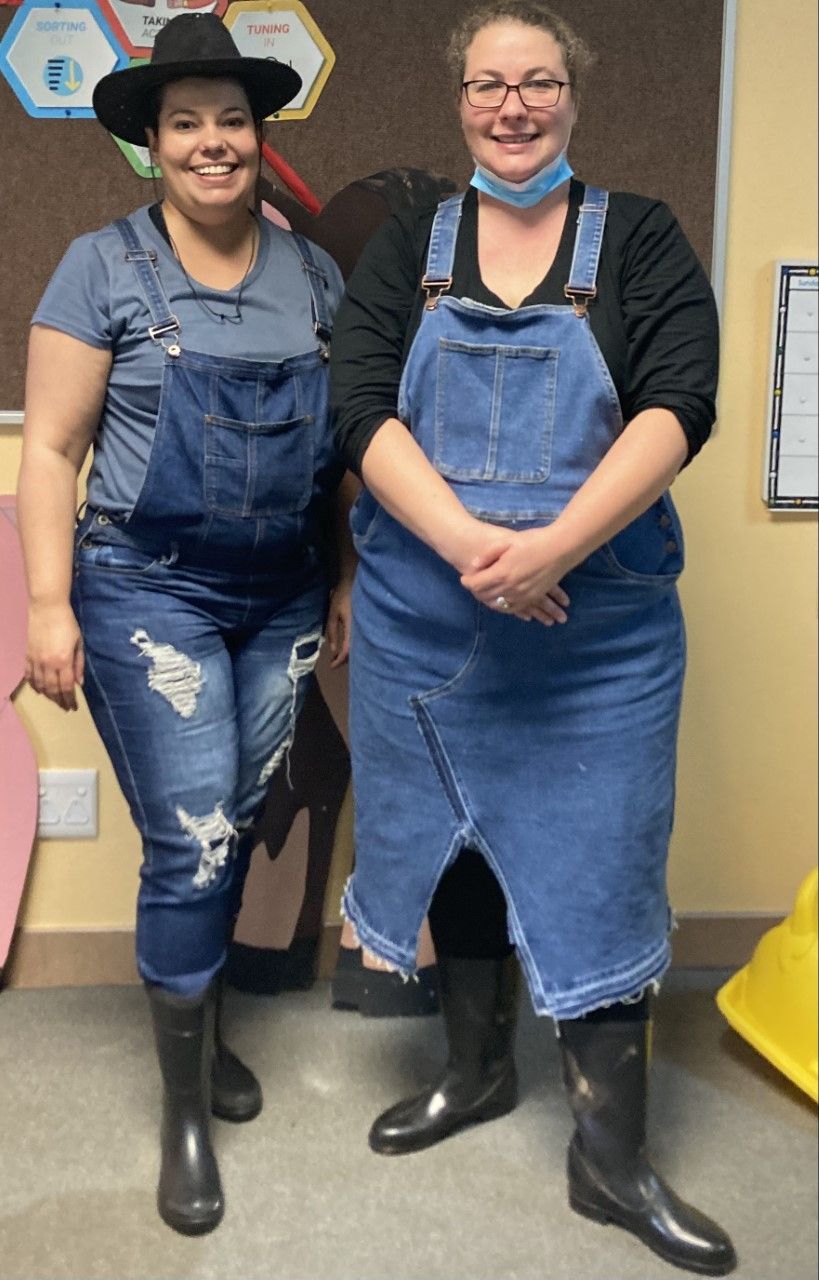 Two women standing next to each other wearing overalls and rain boots