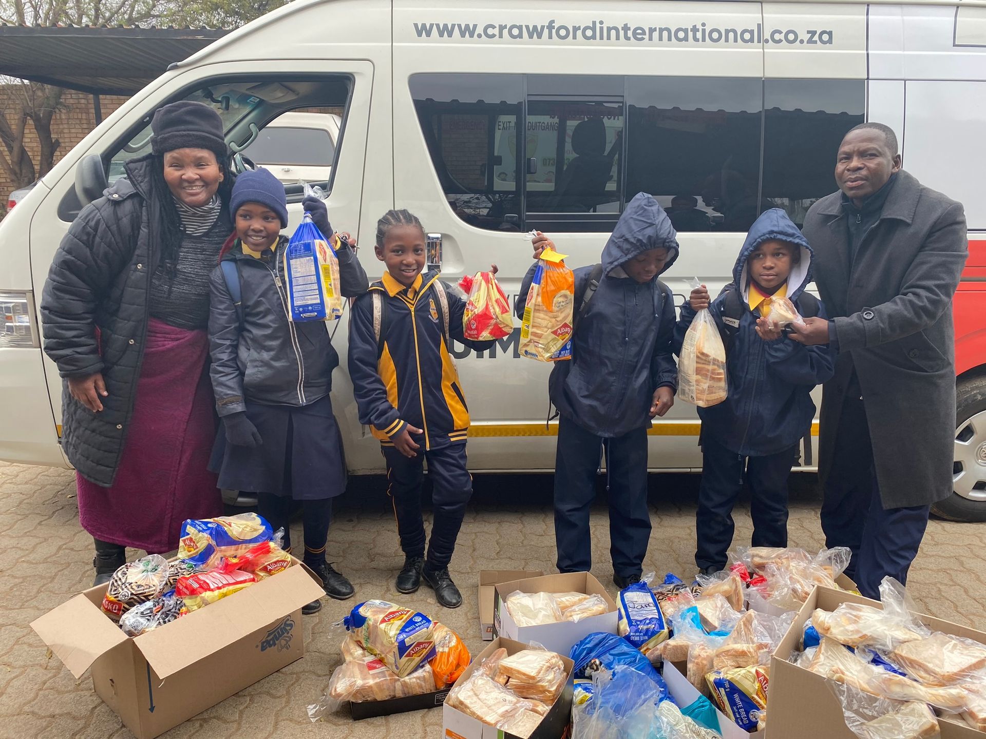 A group of people standing in front of a van holding bags of food.
