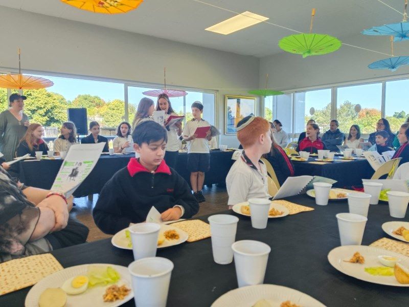 A group of people are sitting around a table with plates of food and cups.