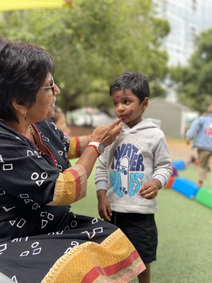 A woman is putting holi paint on a young boy 's face.