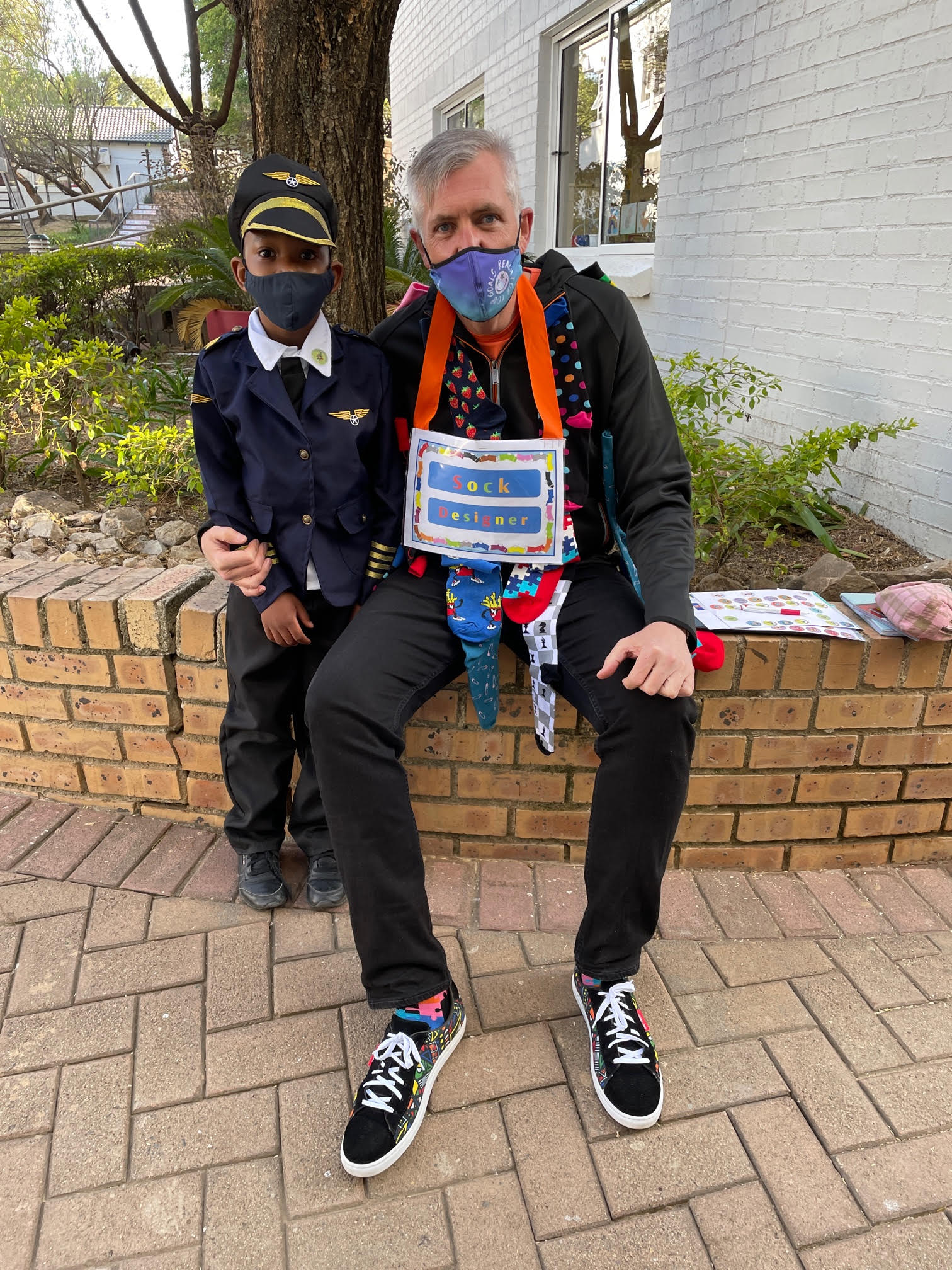 A man and a boy wearing masks are sitting on a brick wall.