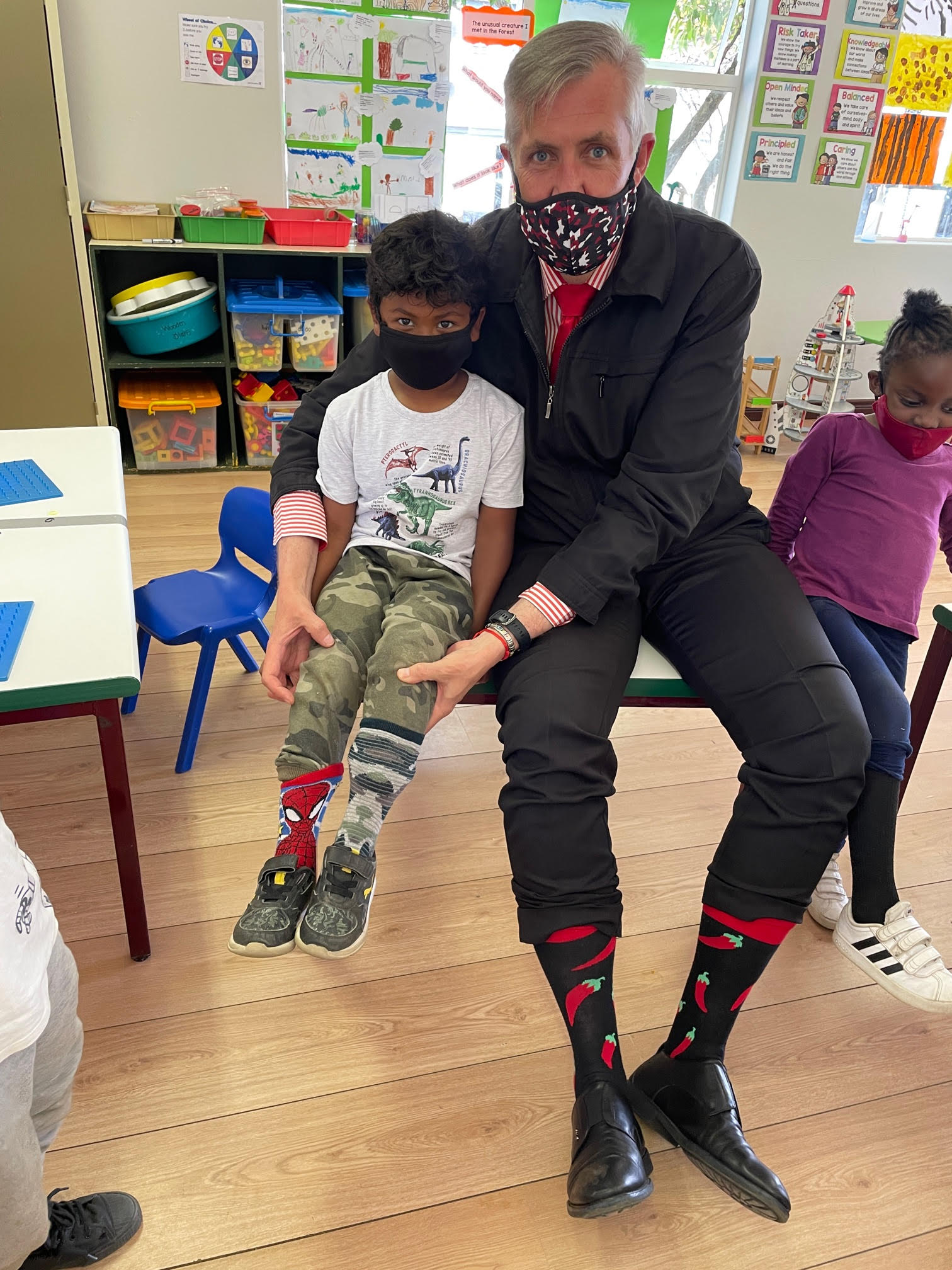 A man wearing a mask is sitting on a bench next to a boy wearing a mask.
