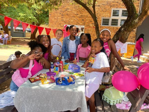 A group of young girls are sitting at a table with pink balloons.