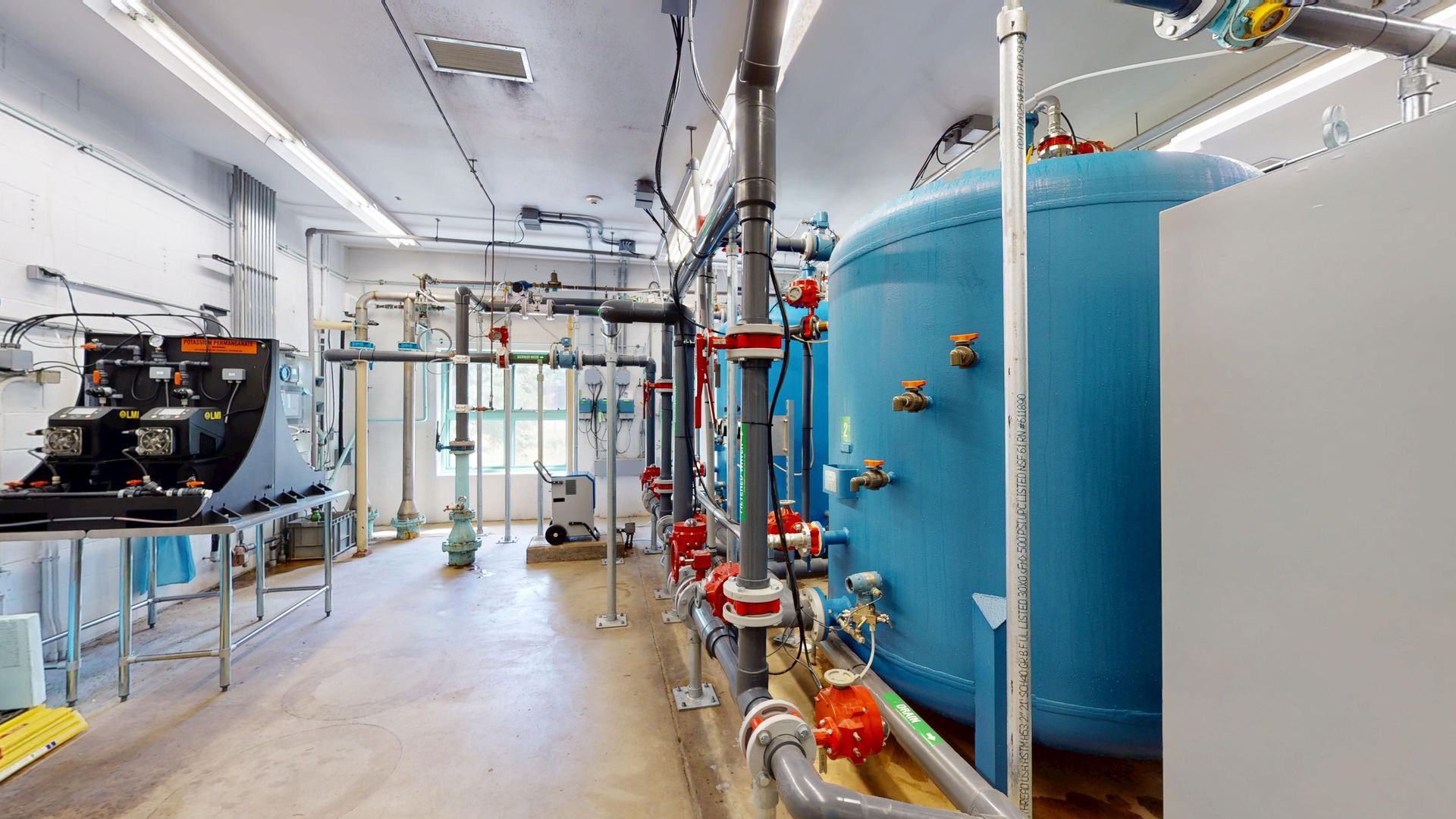 A utility room with blue tank, various pipes and equipment, likely for water treatment or industrial use.