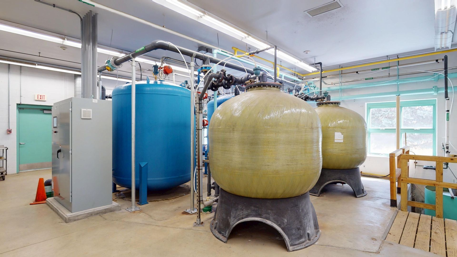 Water treatment facility interior with blue and tan tanks, pipes, and control panel.