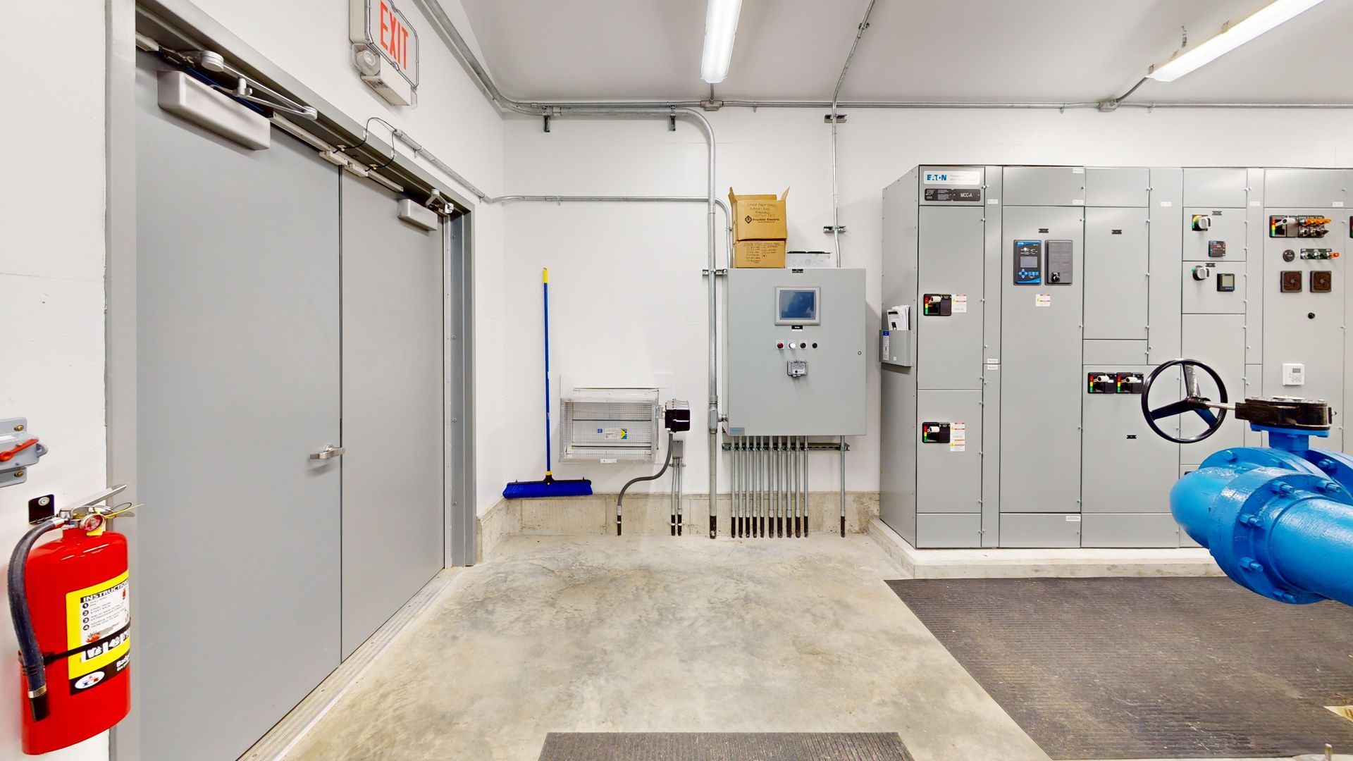 A room with a lot of electrical equipment and a fire extinguisher on the wall.