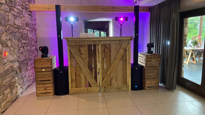 DJ setup in a rustic venue with wooden crates, speakers, lights, and a wooden DJ booth.