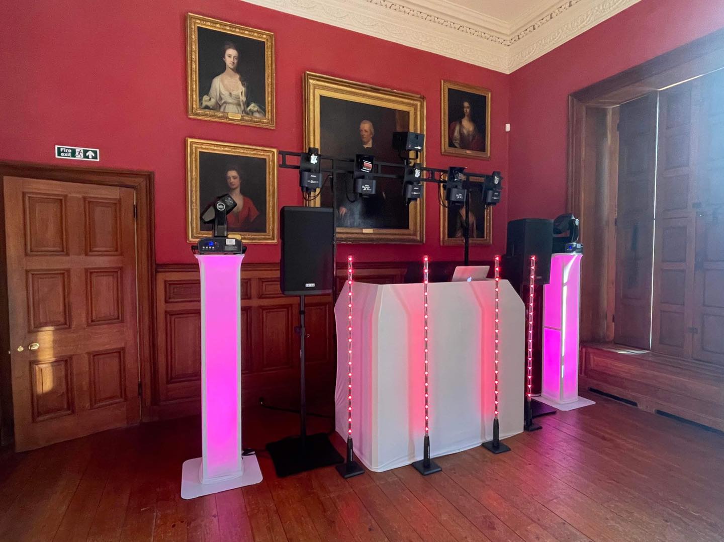 DJ setup in a red-walled room with portraits. Pink lights illuminate the DJ booth and pillars.