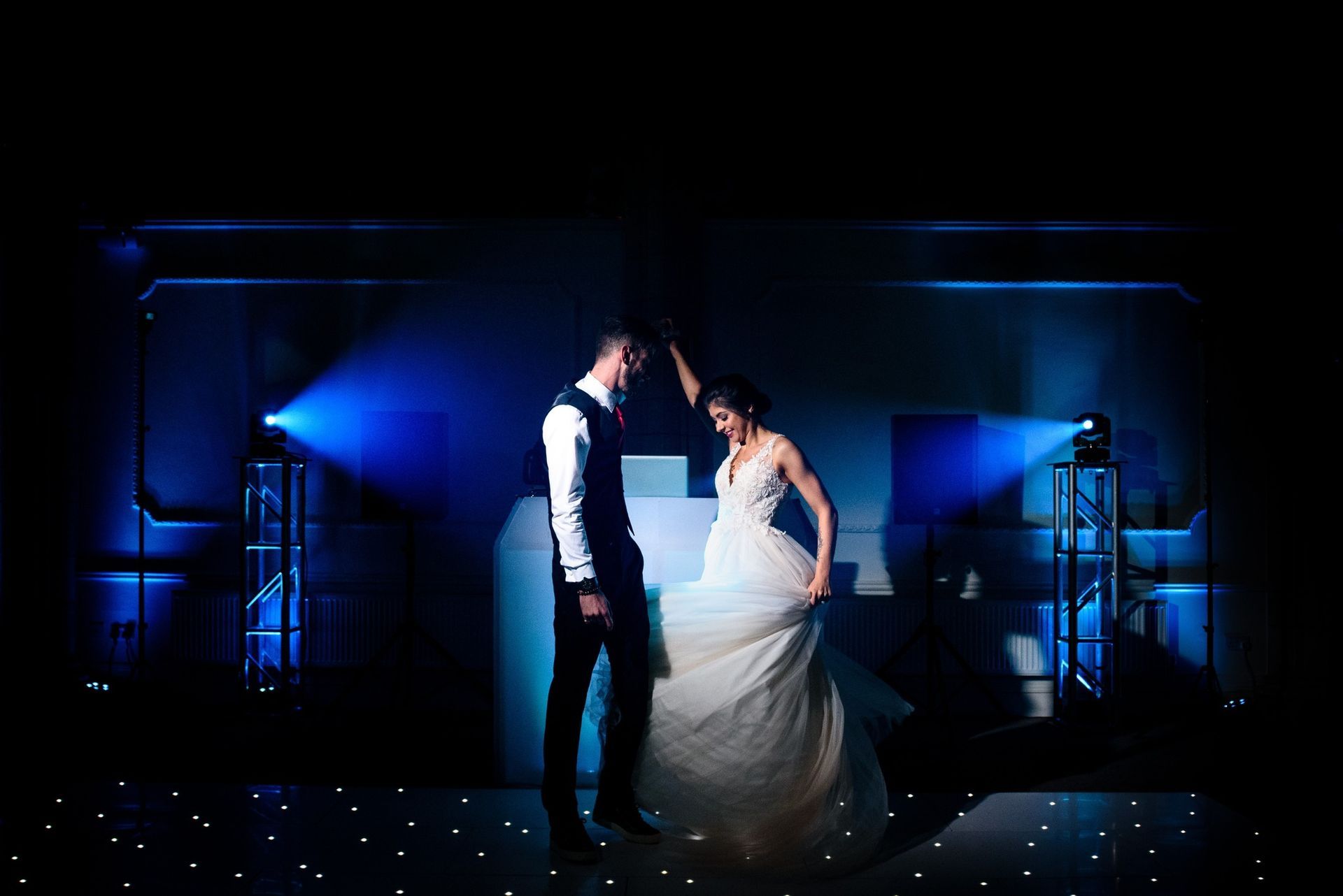 Party setup with illuminated balloons, DJ booth, speakers, and colorful lights in a room with stone walls.
