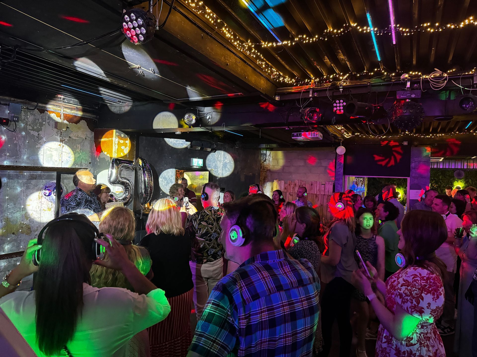 People dancing at a silent disco. Partygoers wear headphones, illuminated by disco lights in a club.