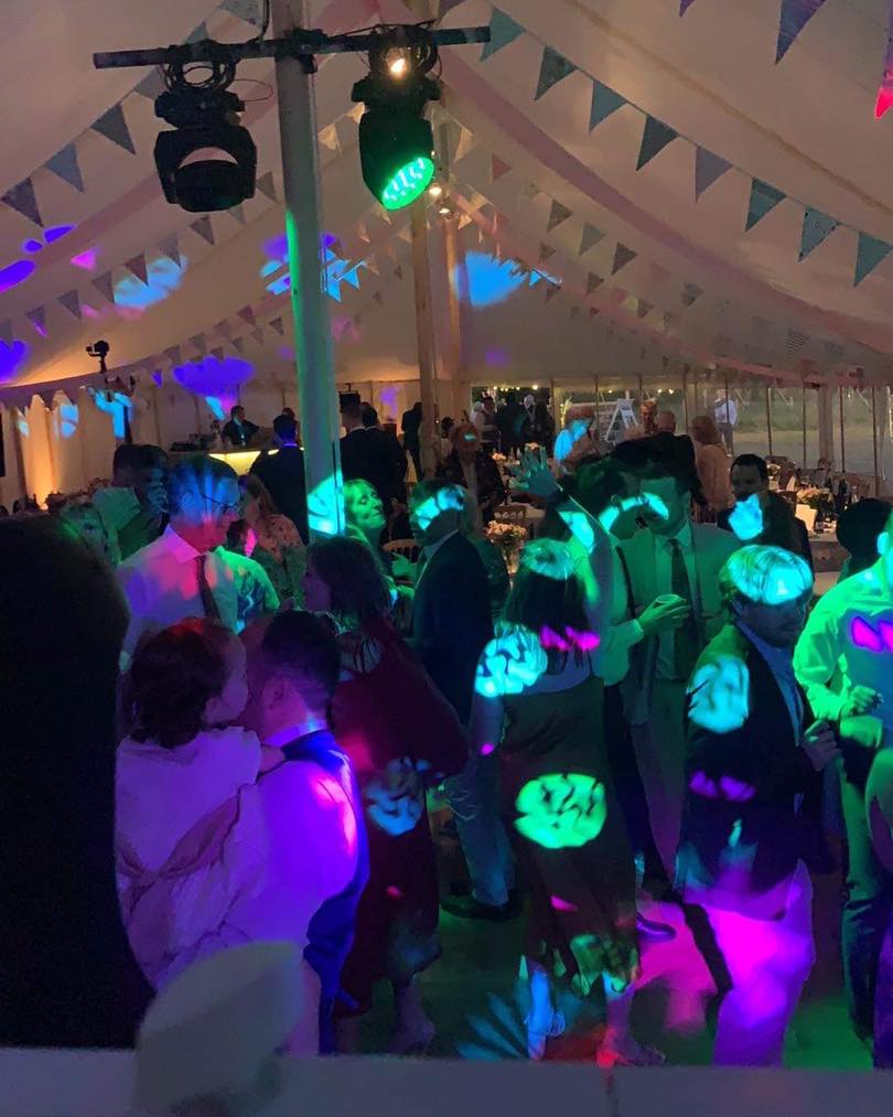Party under a tent with colorful lights, dancing people.