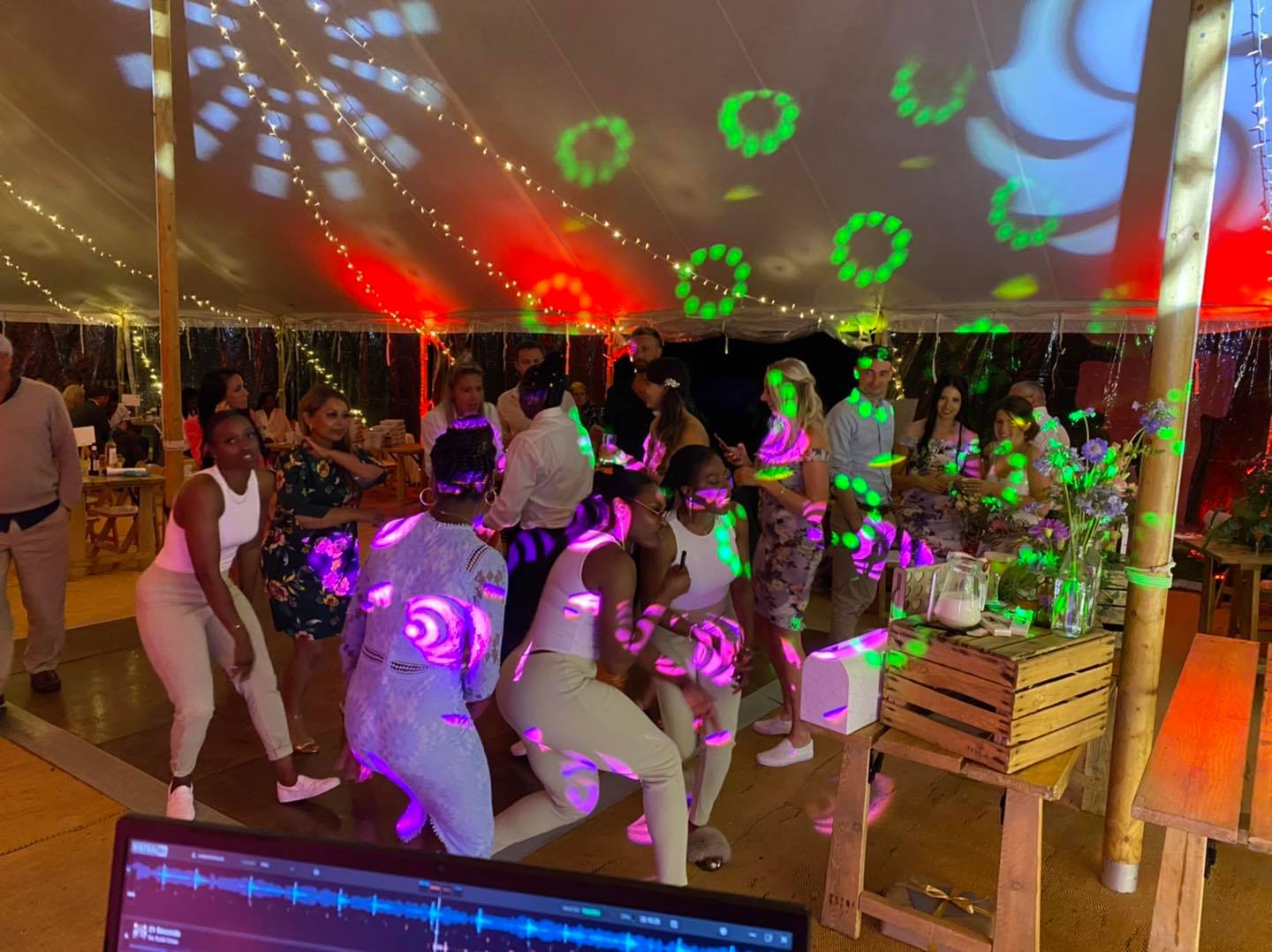 People dancing under colorful lights at a party in a tent.