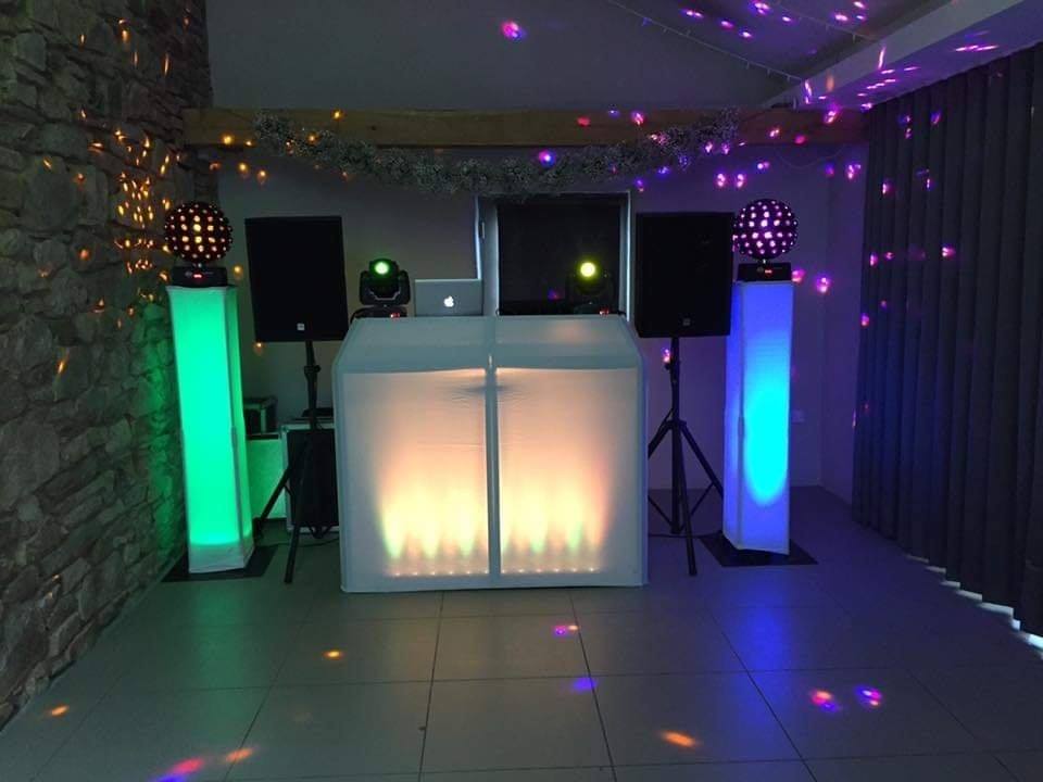 DJ setup with colored lights, speakers, and a white booth.