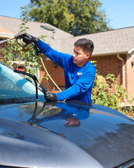 Man polishing a black Toyota SUV outdoors, with a yellow service van and house in the background