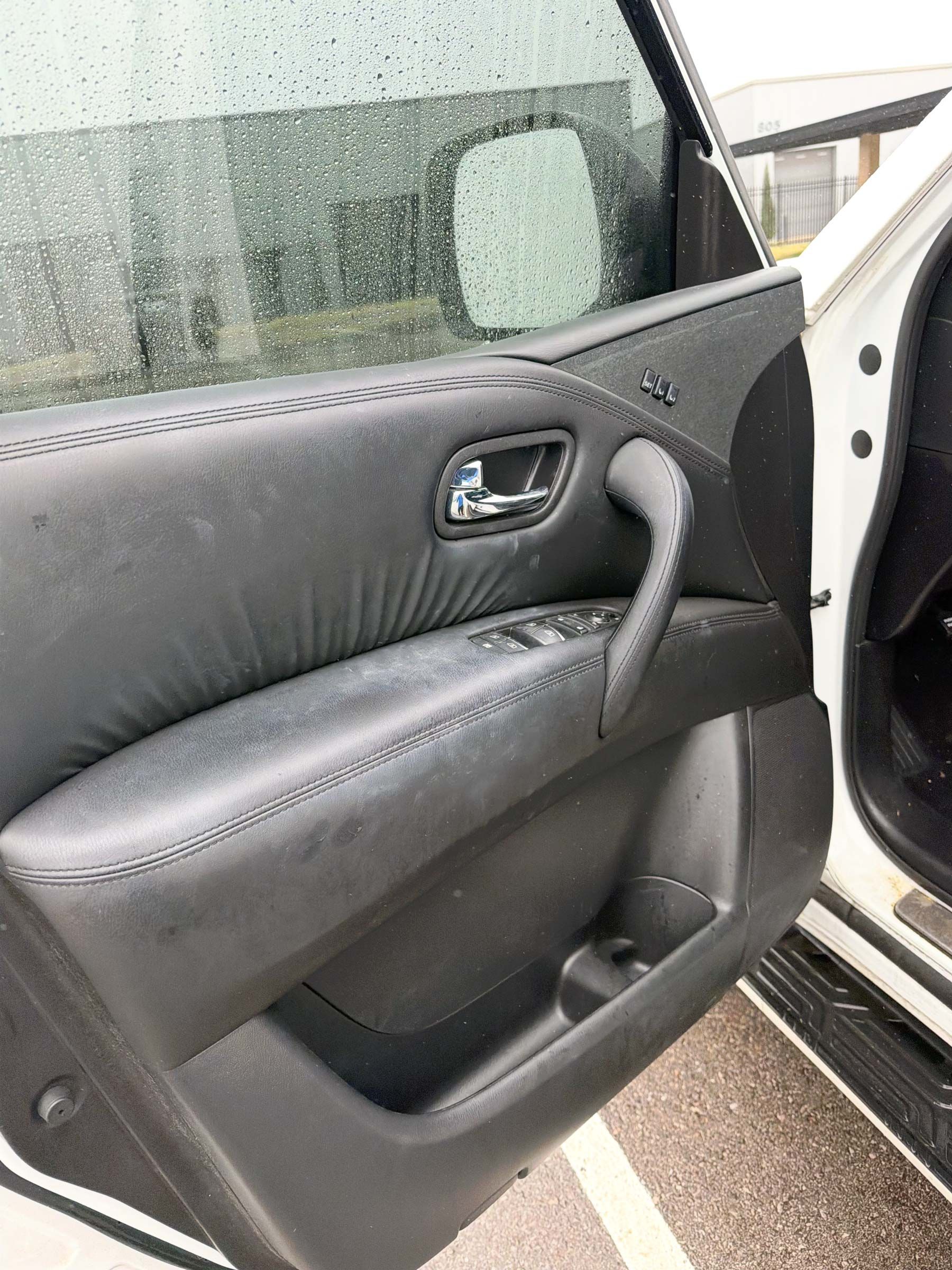 Car door interior with black trim and handle, open to a rainy exterior.