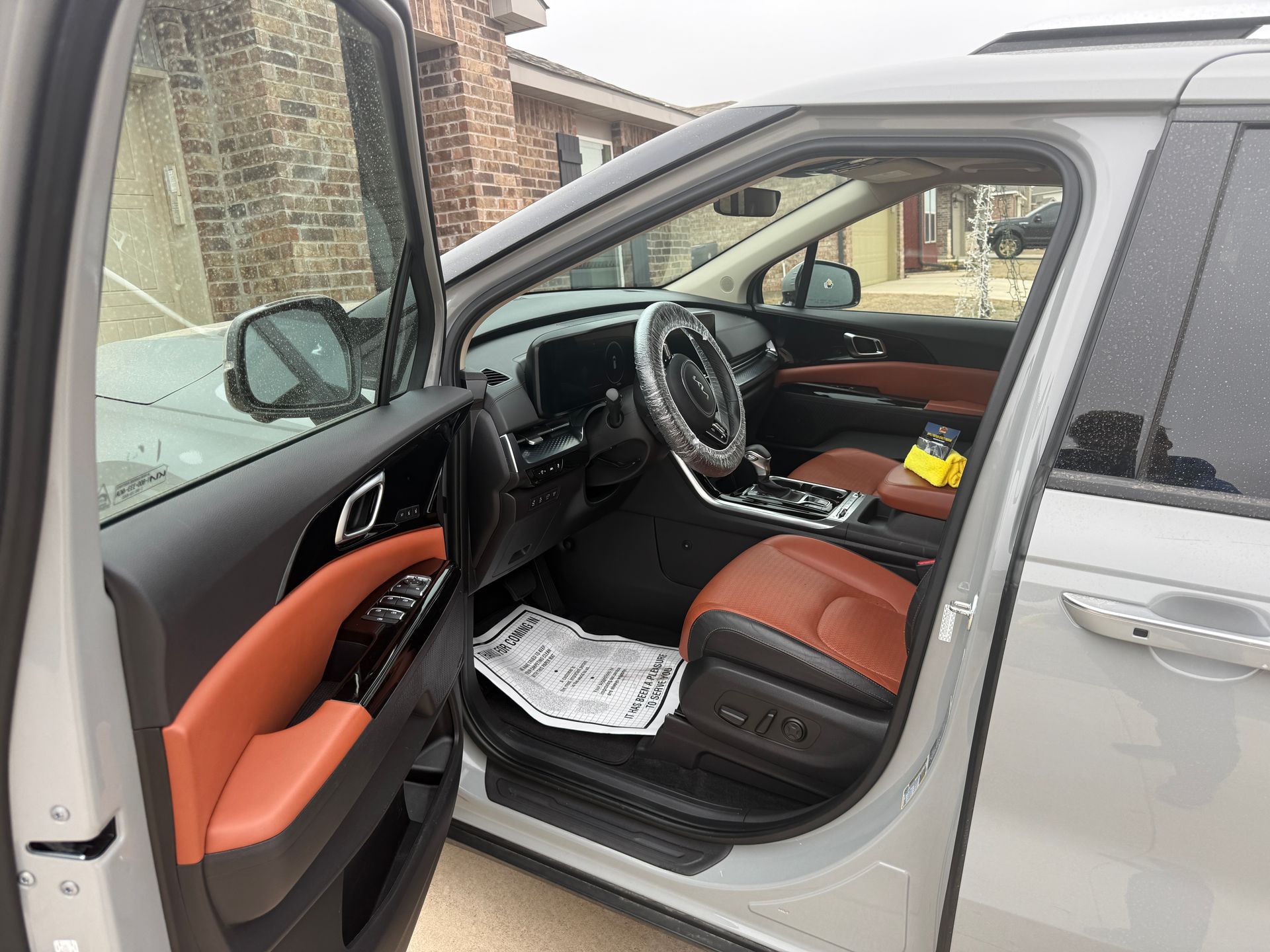 Silver car with open driver door, showing tan and black interior and papers on the floor mat