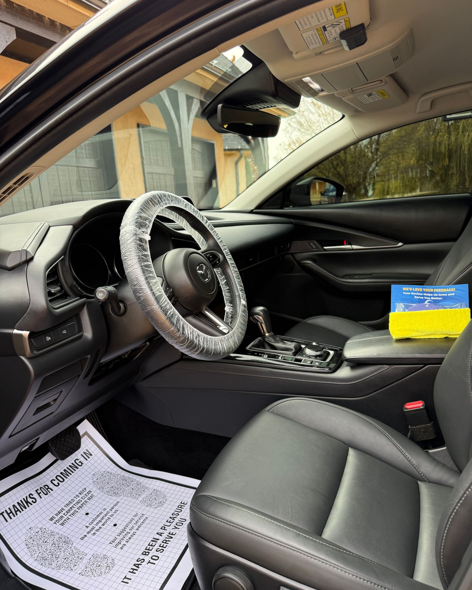 Car interior with steering wheel cover, passenger seat, and papers on the floor, viewed from the open door