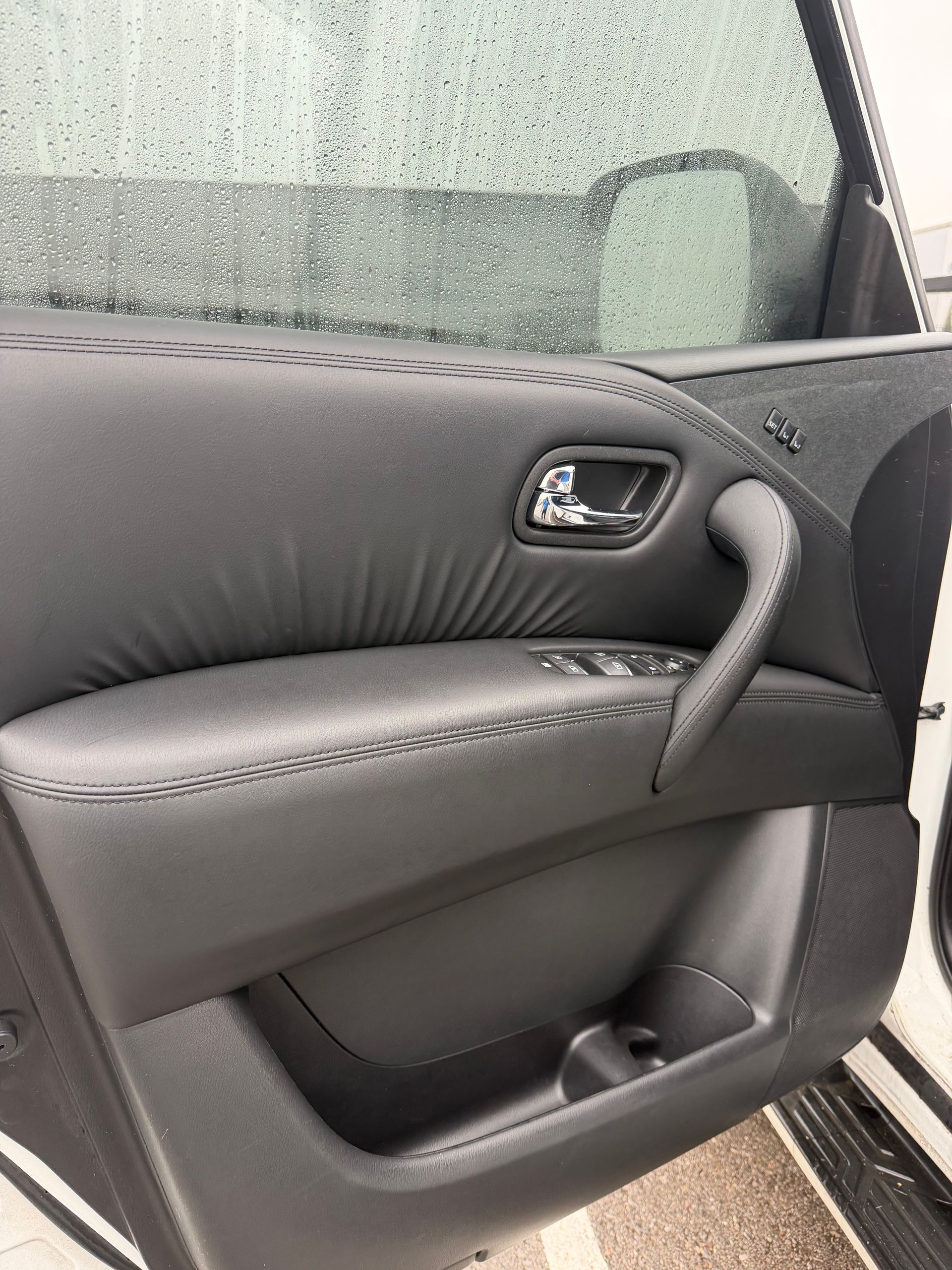 Black car door interior with armrest, handle, window, and storage pocket.